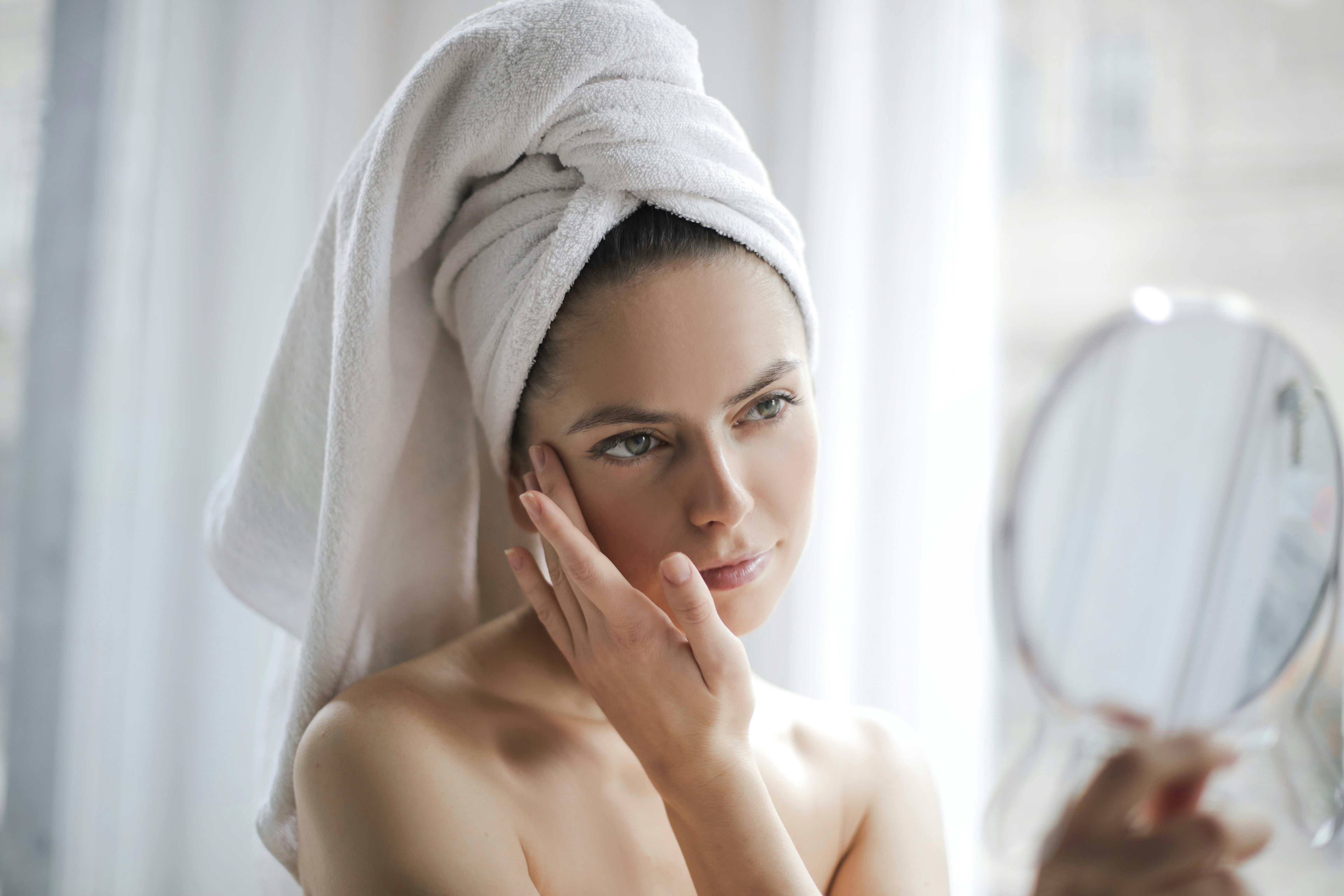woman looking in a mirror examining her skin with some concern 
